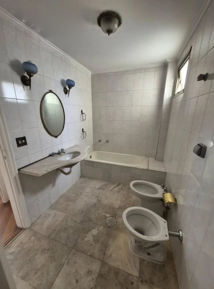 Antes: banheiro antigo com azulejo branco, banheira embutida, bidê e luminárias azuis