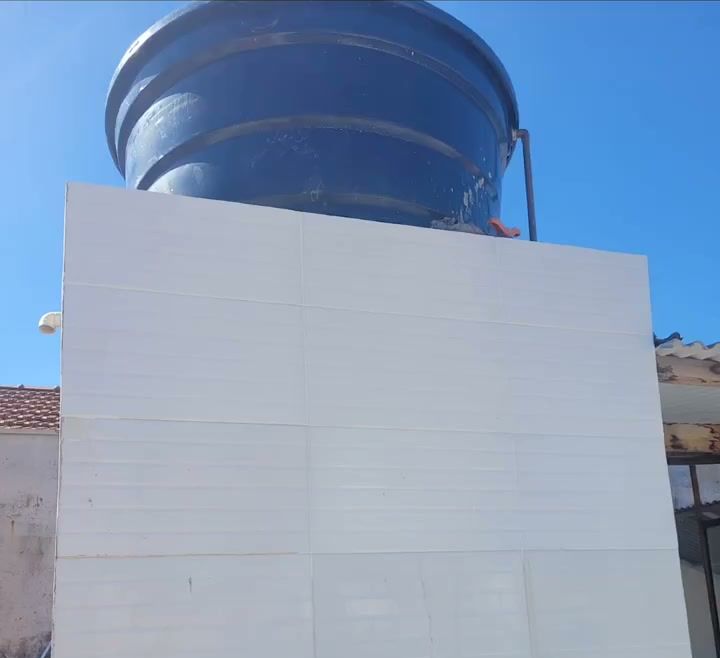 Caixa d'água sobre base nova revestida de branco, em obra de reposicionamento do barrilete