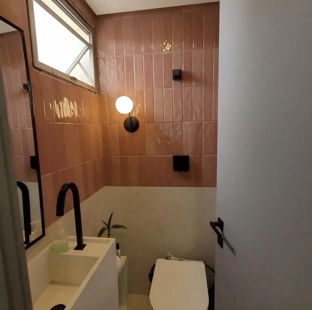 Depois: lavabo com revestimento rosado vertical, metais pretos, arandela e cuba esculpida